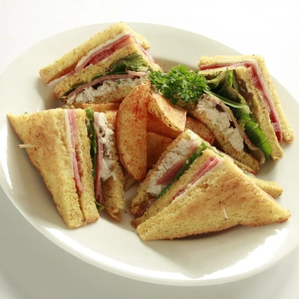 Club sandwiches with ham, chicken, lettuce, and tomato, served with potato wedges and parsley.
