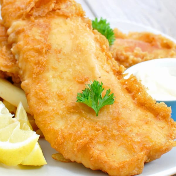 Golden-brown fried fish with lemon wedges, fries, and tartar sauce on a white plate.