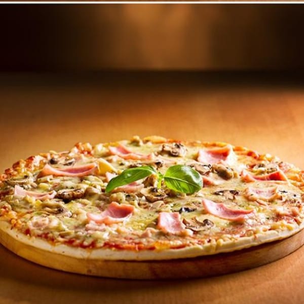 Paramount Pizza 3's ham and mushroom pizza, garnished with fresh basil, on a wooden board.