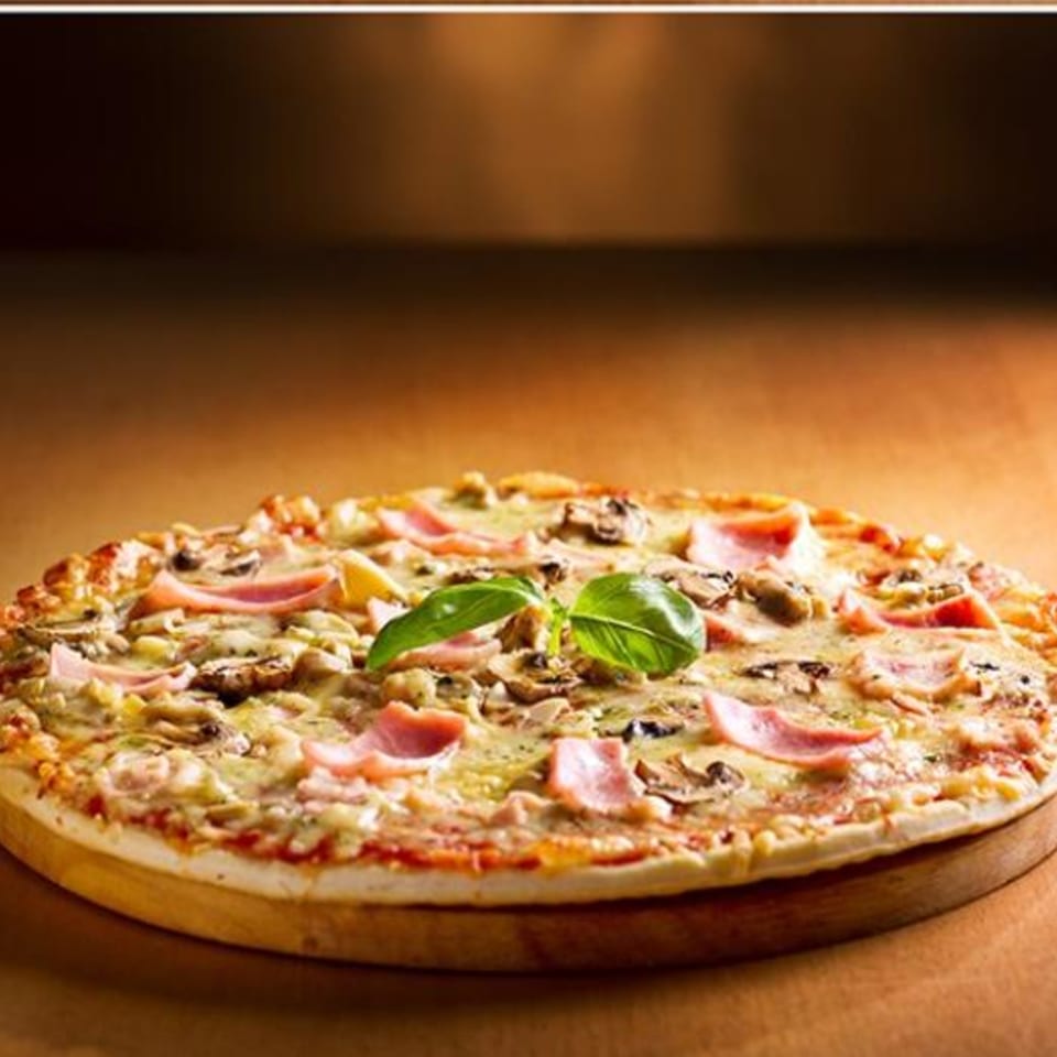 Paramount Pizza 3's ham and mushroom pizza, garnished with fresh basil, on a wooden board.
