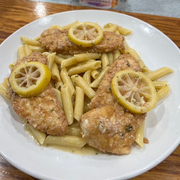 Chicken piccata with penne pasta and lemon slices on a white plate from Paramount Pizza 3.