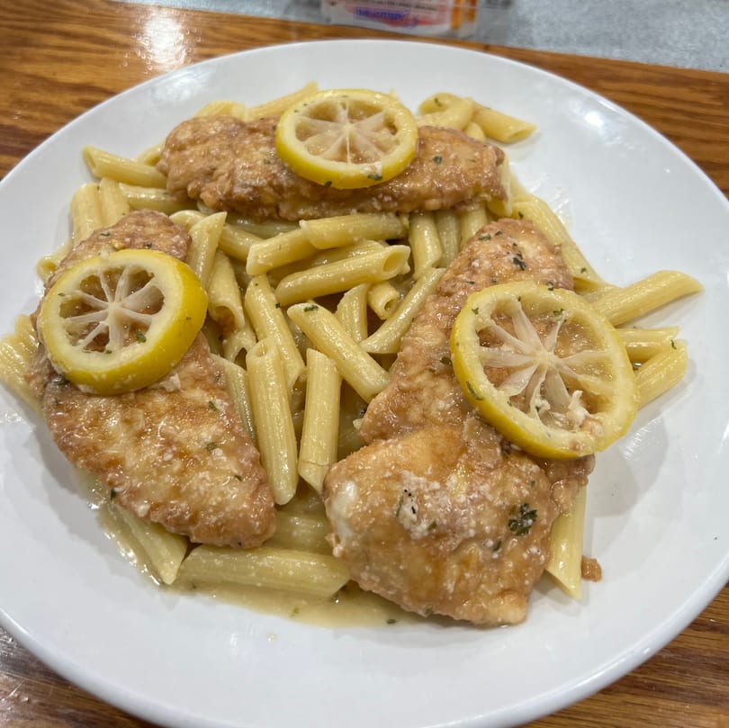 Chicken piccata with penne pasta and lemon slices on a white plate from Paramount Pizza 3.