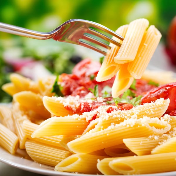 A fork lifts penne pasta from a plate with red sauce, parmesan, and green garnish.